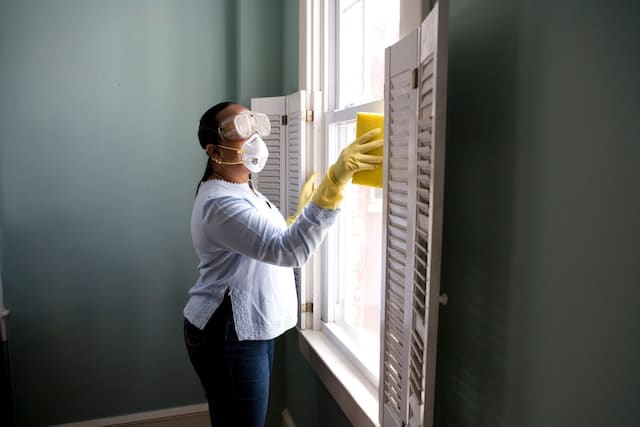 a commercial cleaning woman is washing a window while wearing safety glasses and mask