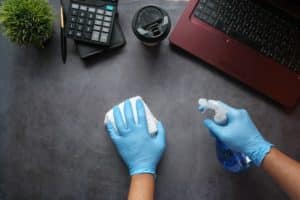 person wearing gloves cleaning a desk in an office