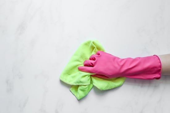a person wearing a pink rubber glove with a light green rag wiping a counter