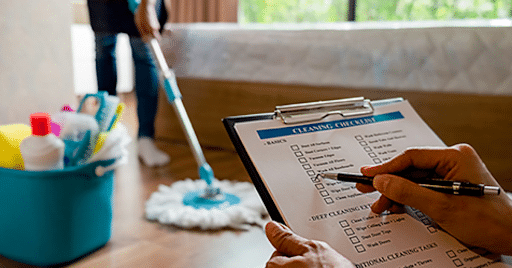a person holding a cleaning checklist with cleaning supplies in the background