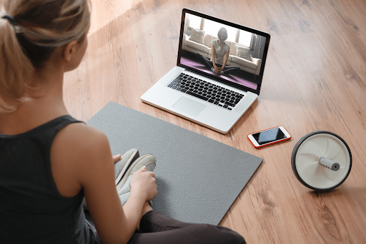 a woman on a yoga mat following a video on her laptop in front of her