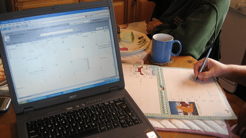 person writing on a calendar with a laptop open