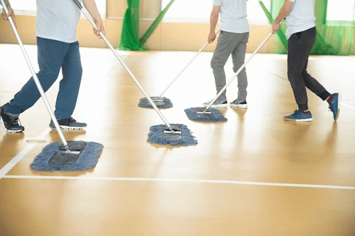 4 people pushing brooms on a gym floor