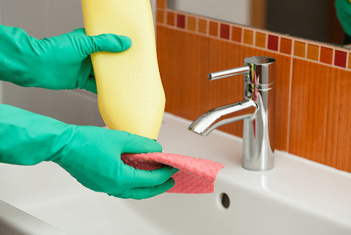 Cleaning product being put on a red towel being prepared by person wearing green gloves over a white sink