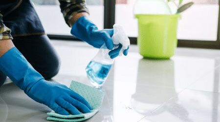 a person wearing blue rubber gloves with cleaning spray and a rag wiping the floor
