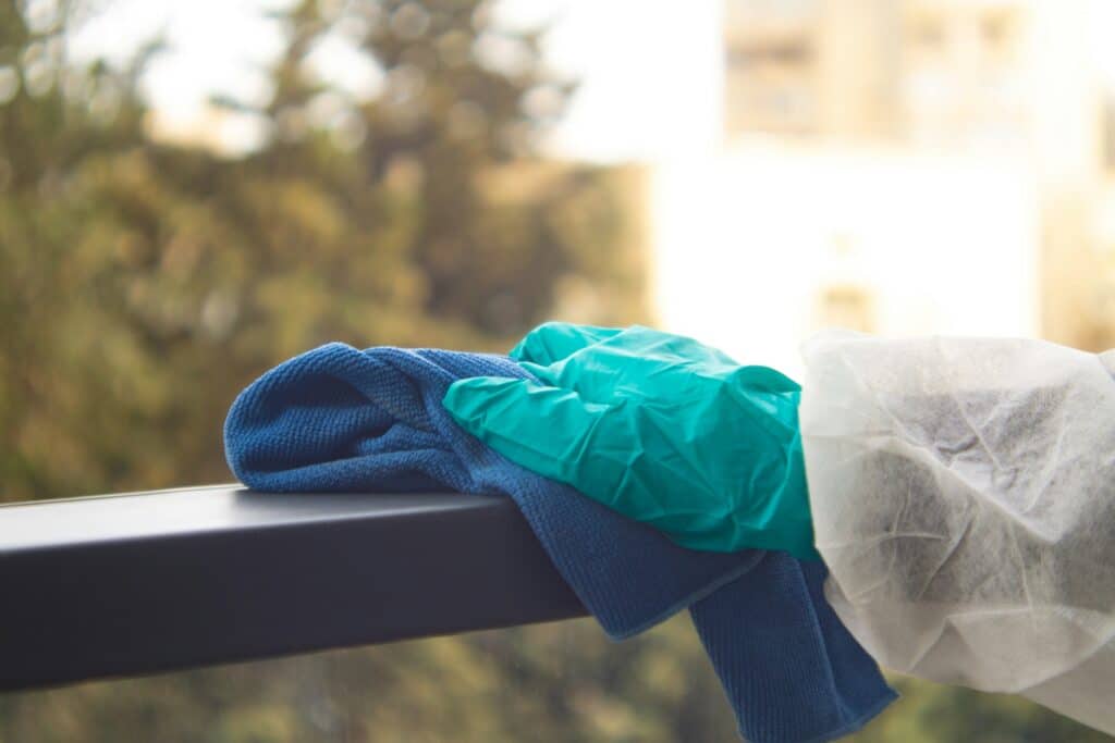 cleaning a railing with a blue rag, while wearing a turquoise glove and protective clothing