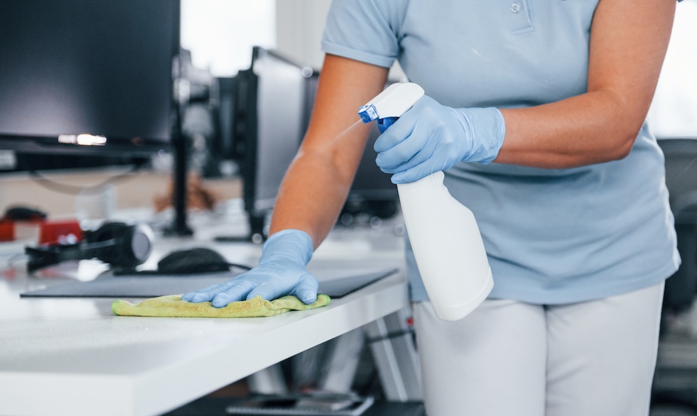 Woman in protective gloves that cleaning tables in the office.