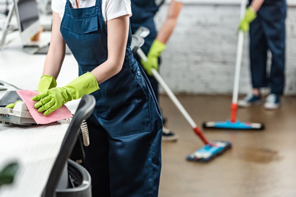 cleaner wiping phone while colleagues washing floor with mops