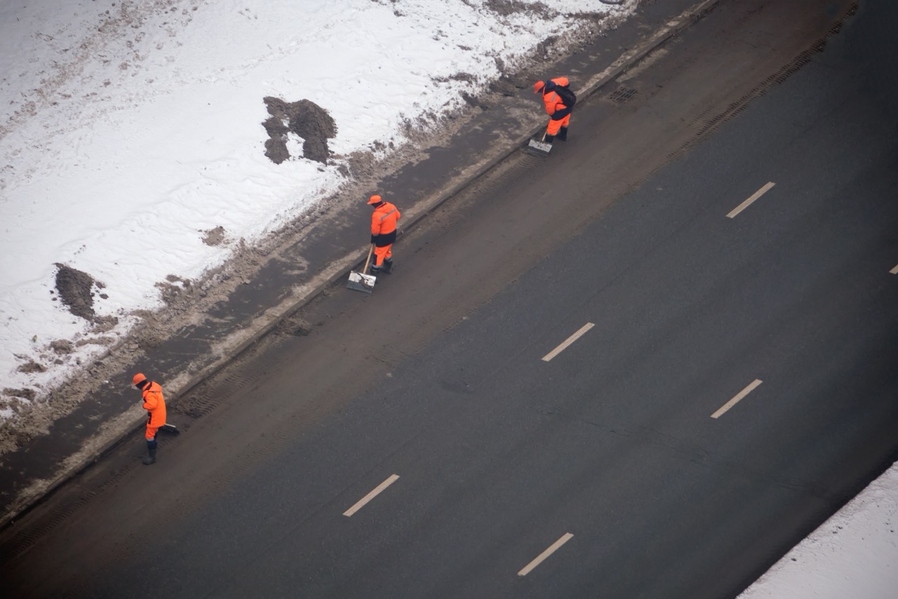 Three,Workers,In,Orange,Uniforms,Clearing,Snow,From,The,Roadside