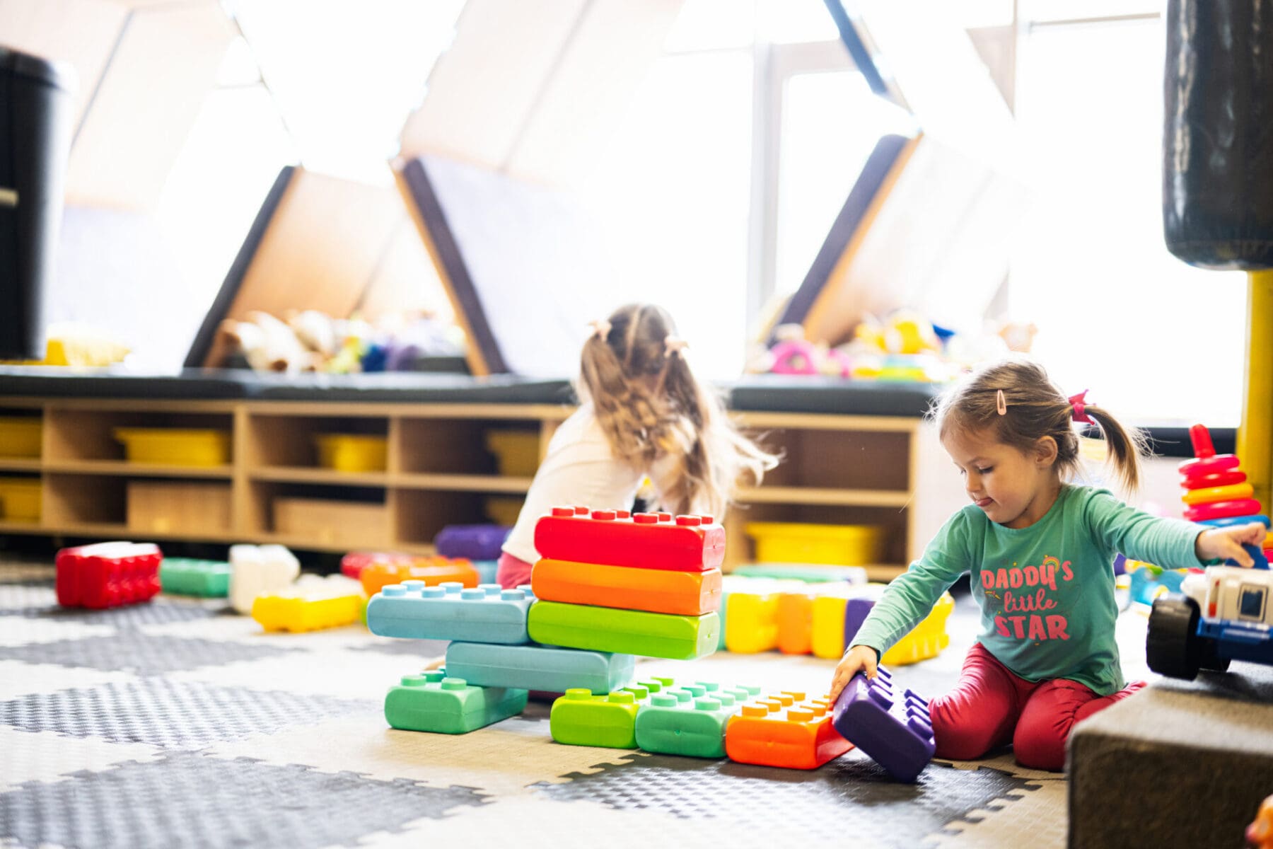 Two sisters playing at kids play center while build with colored daycare cleaning kids